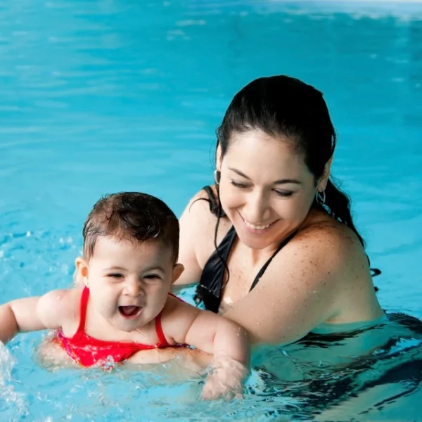 Swim instructor giving early swim lessons for kids, by guiding an infant during a water safety progress milestone in a pool.