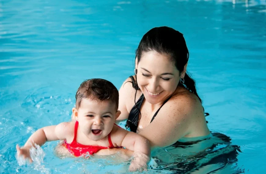 Swim instructor giving early swim lessons for kids, by guiding an infant during a water safety progress milestone in a pool.