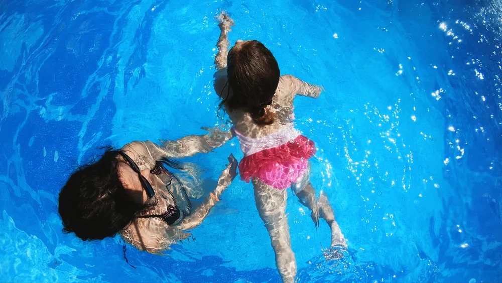 Early Swim Lessons for Kids: How Water Supercharges the Growing Brain 3 Swim teacher helping kids practice breathing and floating drills to build pool lap confidence.